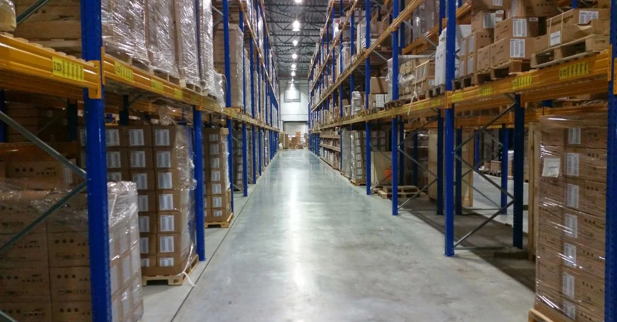 Vue intérieure d'un large couloir d'entrepôt bordé de piles de cartons organisées.