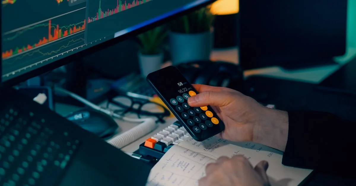 Analyse commerciale à l'aide d'une calculatrice et d'un écran d'ordinateur affichant des graphiques et des tableaux financiers.