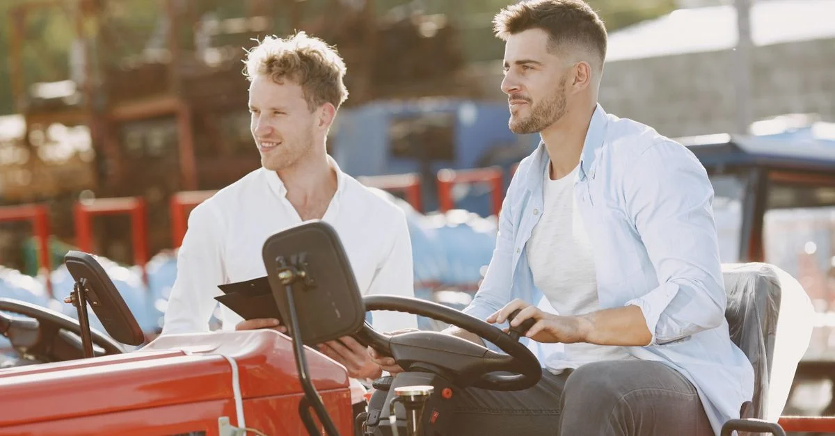 Deux hommes discutent des ventes tout en inspectant un tracteur en plein air. Idéal pour des thèmes commerciaux et agricoles.