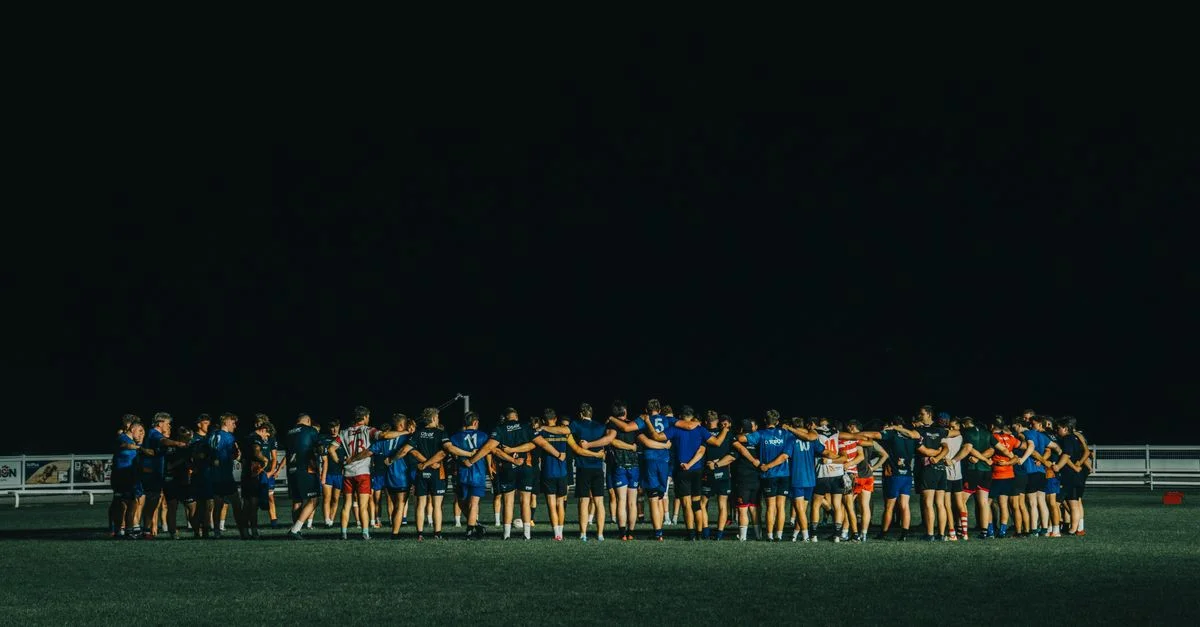 Une équipe sportive se réunit sur un terrain la nuit, favorisant le travail d'équipe et l'unité.