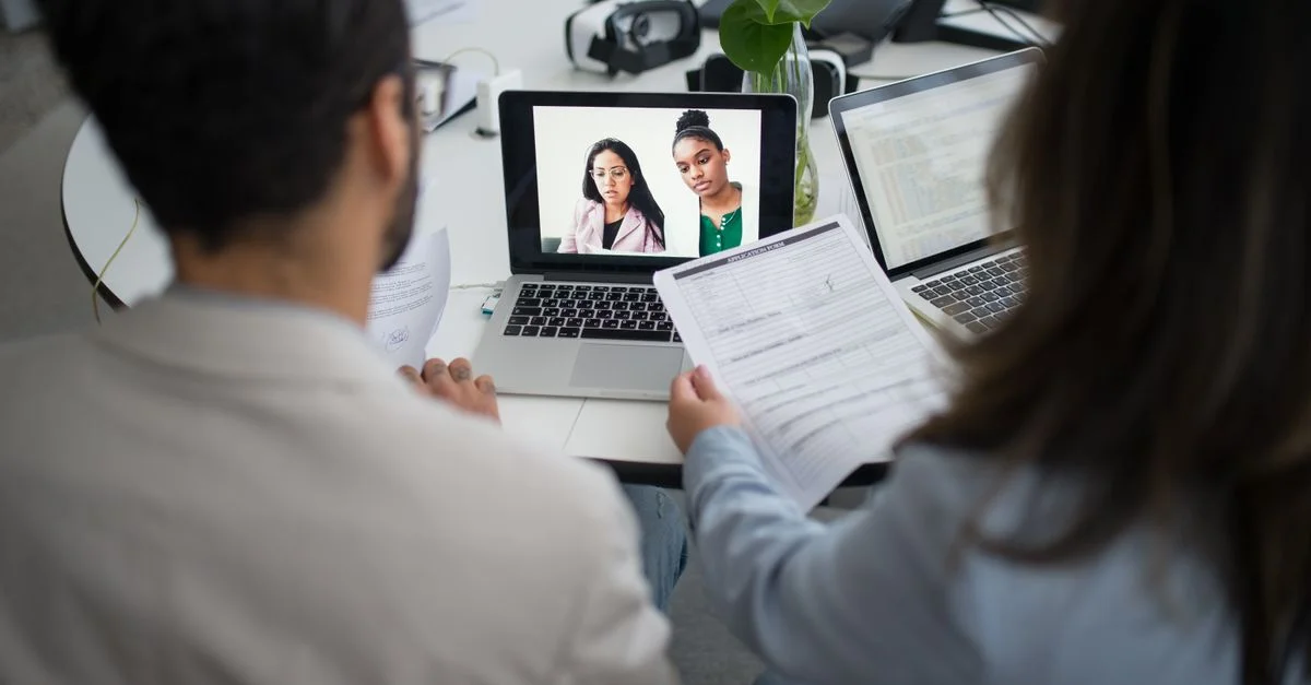 Deux professionnels réalisent un entretien d'embauche virtuel à l'aide d'ordinateurs portables dans un bureau moderne.