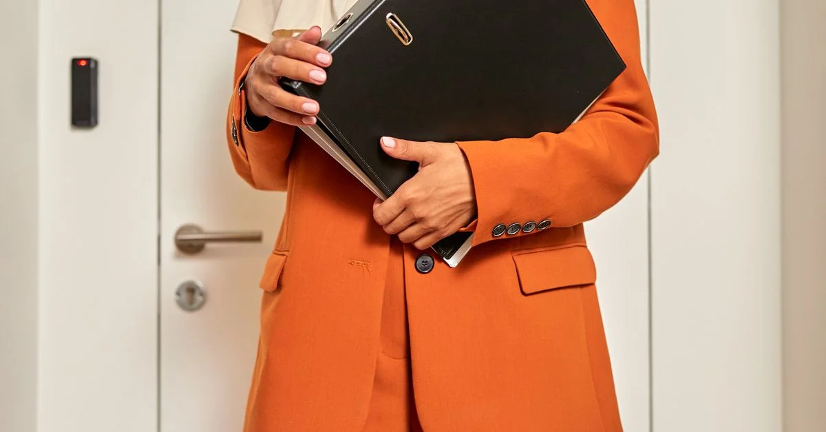 Gros plan d'une femme de bureau tenant un dossier tout en se tenant devant une porte fermée.