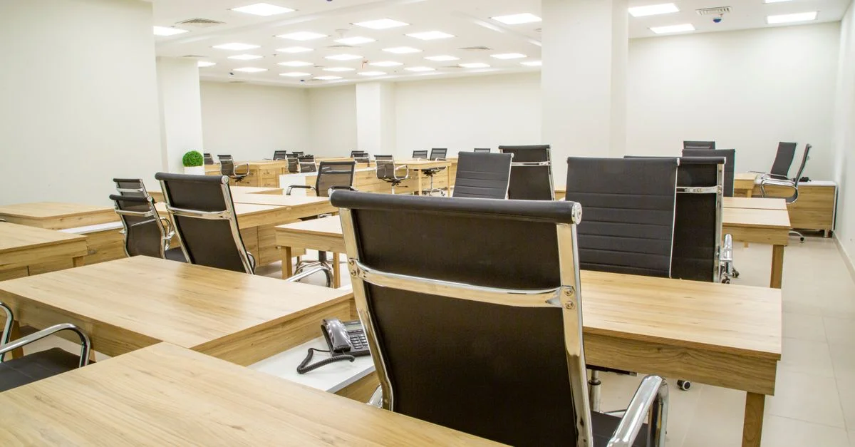 Bureau moderne spacieux avec des bureaux en bois et des chaises en cuir dans une pièce lumineuse et bien éclairée.