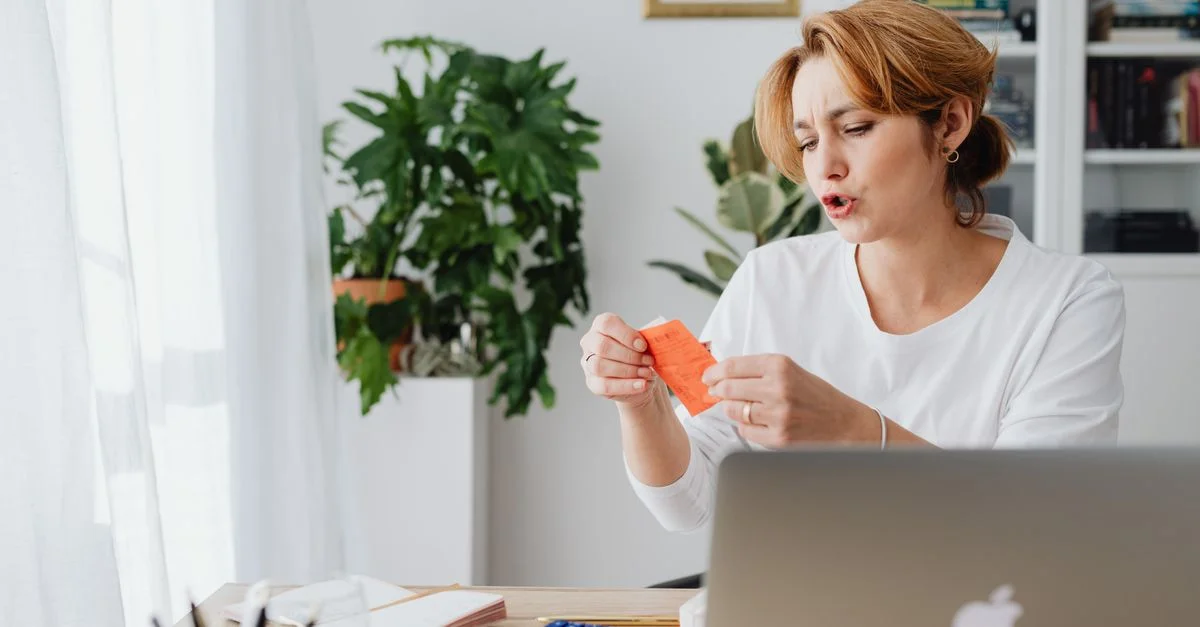 Femme passant en revue ses factures à son bureau à domicile avec un ordinateur portable et des plantes, gérant ses finances personnelles.