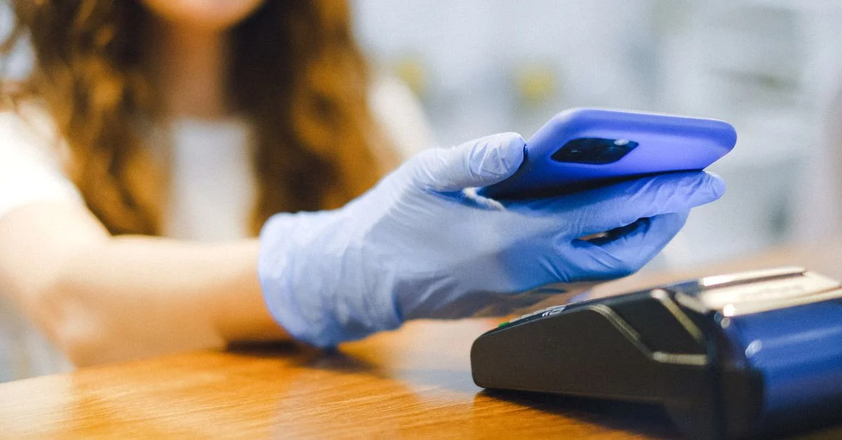 Femme utilisant un smartphone pour un paiement sans contact dans un magasin tout en portant des gants de protection.