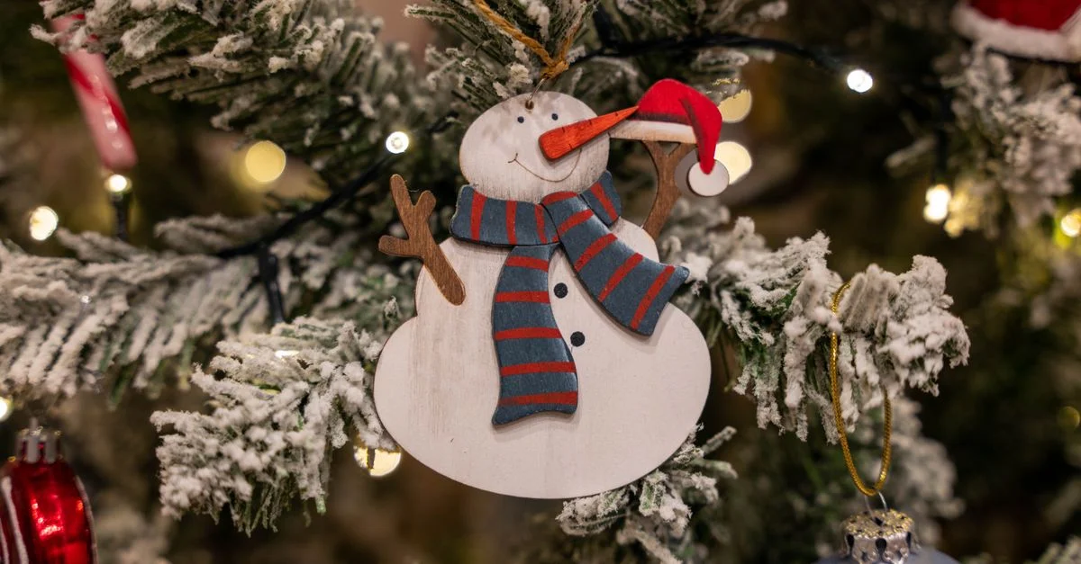 Gros plan d'un ornement bonhomme de neige sur un sapin de Noël floqué, illuminé avec des lumières de fête.