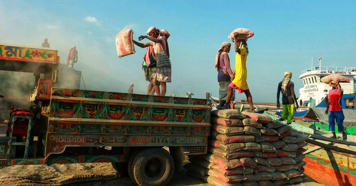 Des travailleurs déchargeant des sacs d'un camion coloré au bord de l'eau, illustrant le travail en équipe et le labeur.