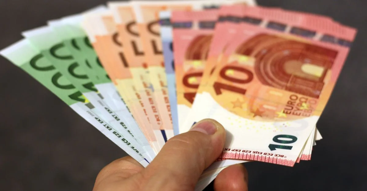Un éventail de billets en euro de différentes dénominations tenu dans une main.