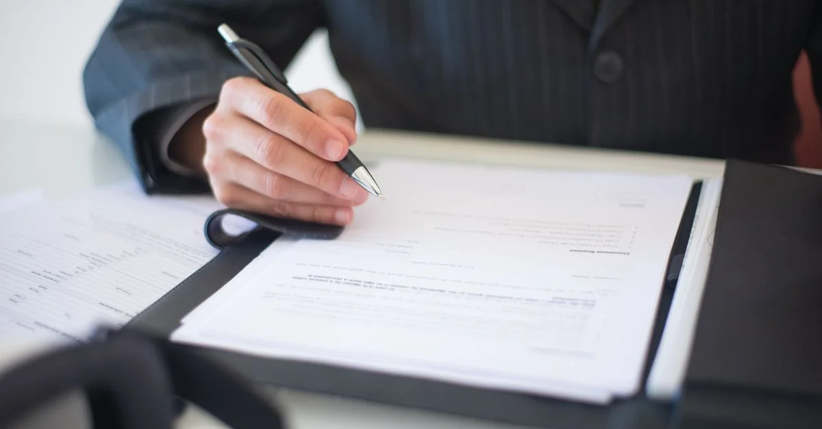 Gros plan d'une main signant des documents avec un stylo, symbolisant un contrat d'affaires important.
