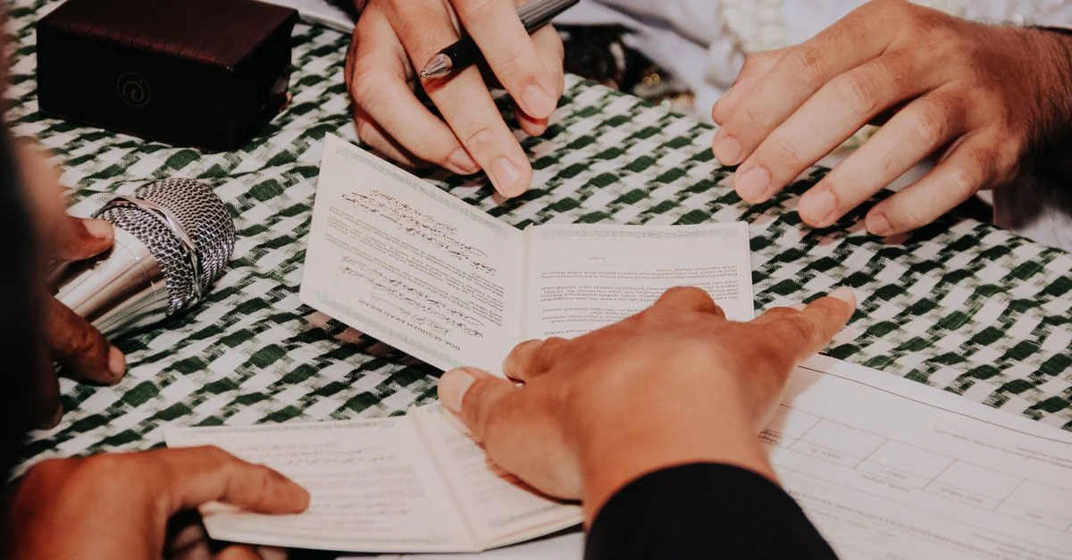 Plusieurs mains tenant et signant un document lors d'une cérémonie formelle avec un microphone à proximité.