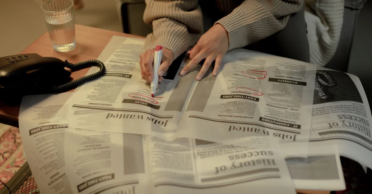 Une femme adulte marque des offres d'emploi dans un journal tout en étant assise à l'intérieur, mettant en évidence l'activité de recherche d'emploi.