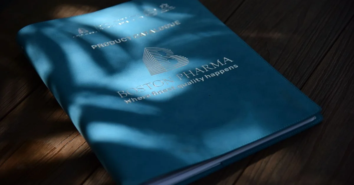 Un dossier bleu portant le logo de Boston Pharma, à la lumière naturelle sur une surface en bois.
