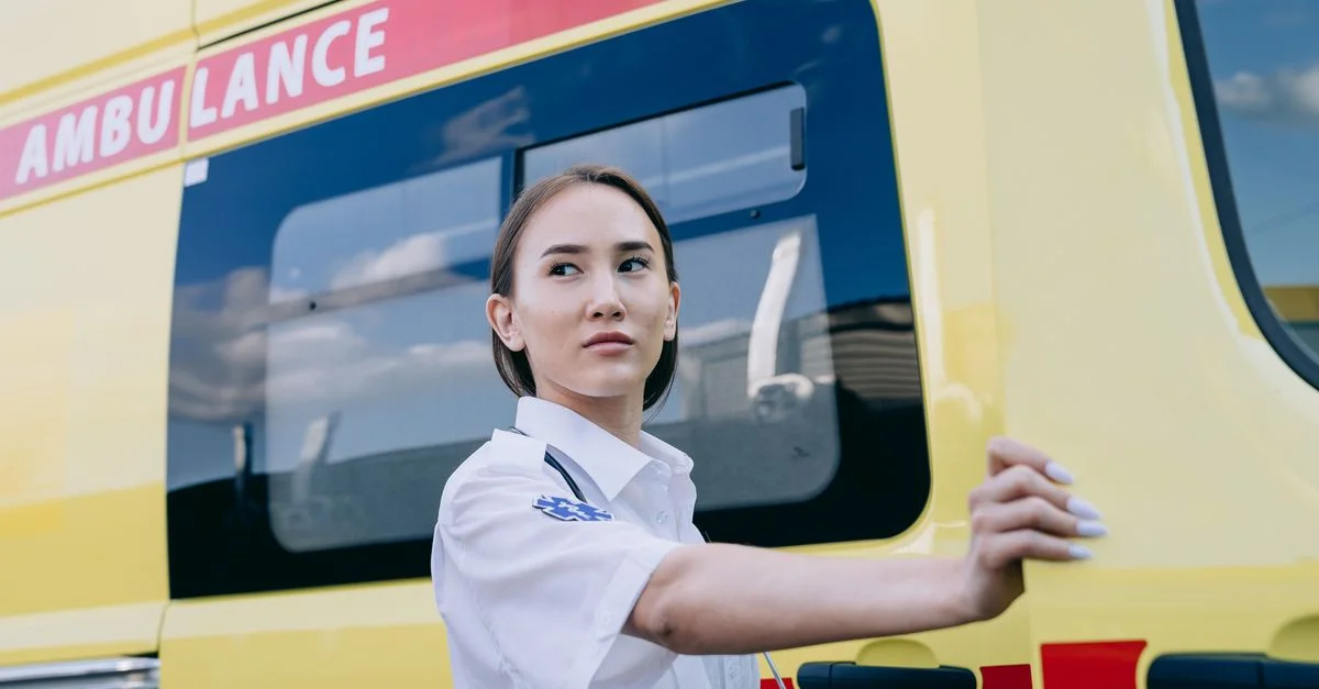 Un ambulancier concentré en uniforme se tenant à côté d'une ambulance jaune vif.