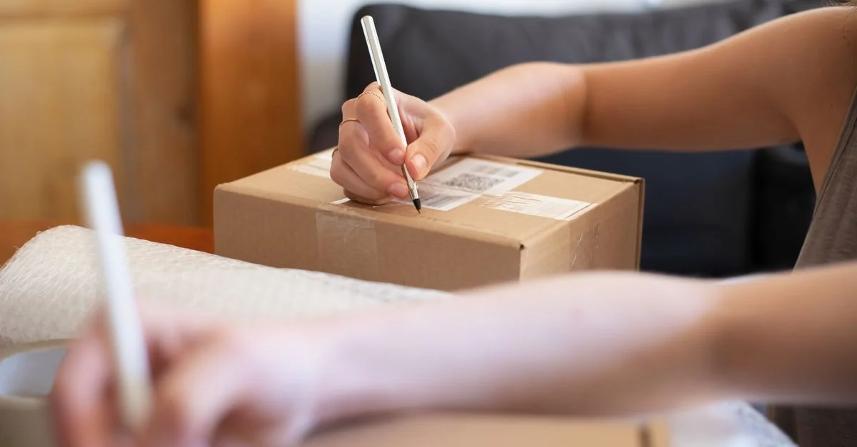Gros plan sur des mains étiquetant une boîte en carton pour un envoi en ligne depuis un bureau à domicile.