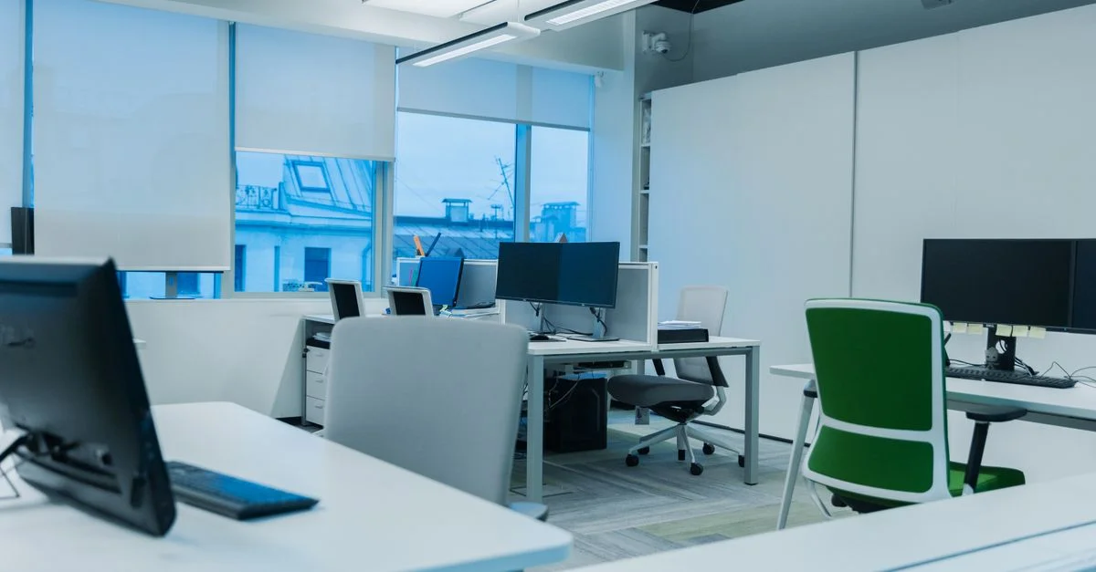 Environnement de bureau lumineux et moderne avec des postes de travail informatiques et de grandes fenêtres.