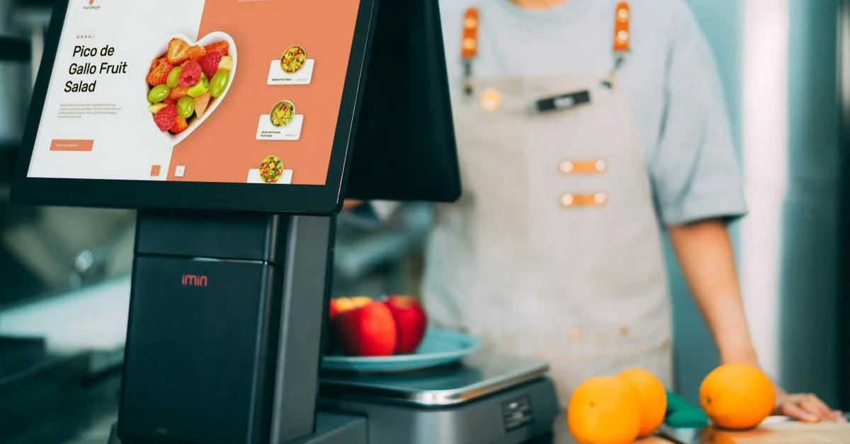 Système de caisse numérique en service dans un supermarché avec des fruits frais et une caissière en vue.