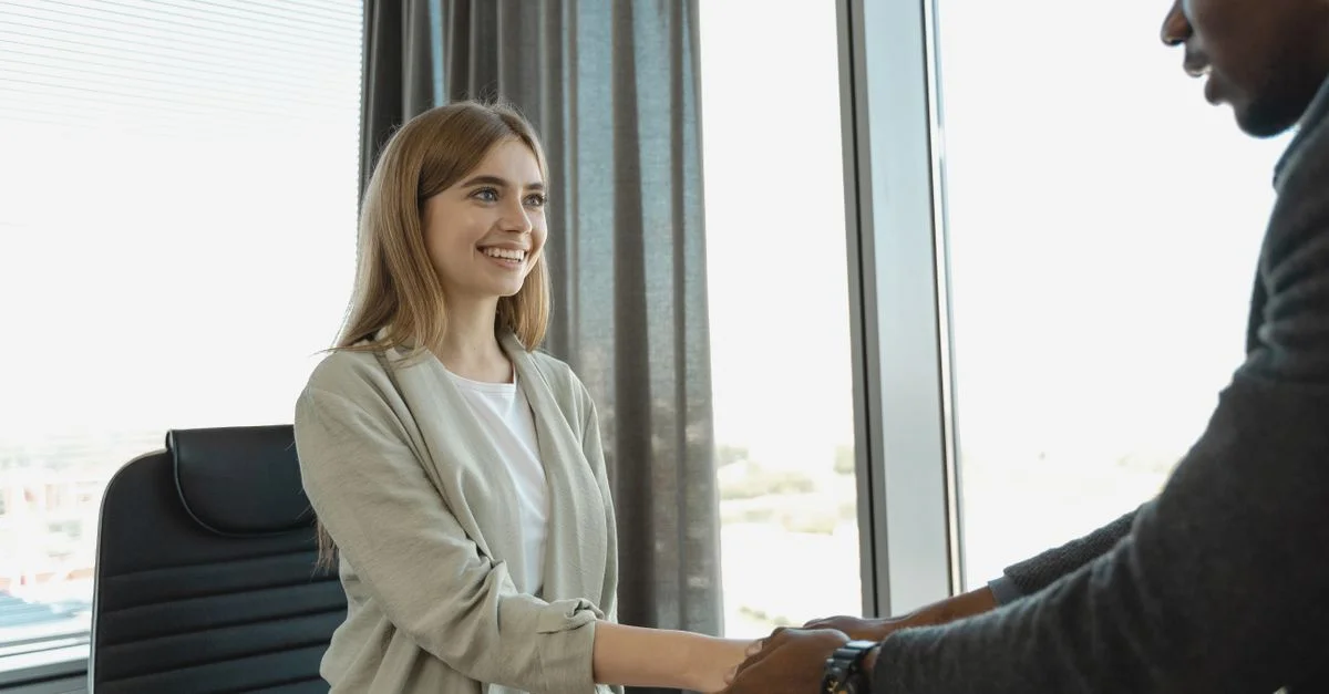 Femme souriante et serrant des mains dans un bureau, signalant un entretien d'embauche réussi.