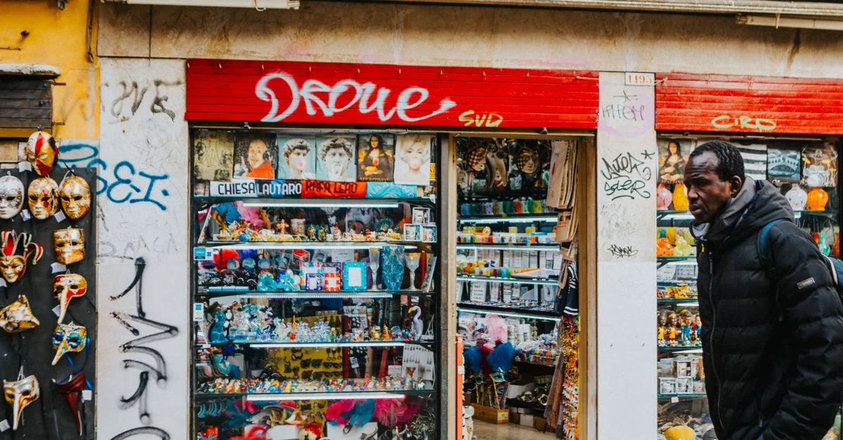 Rue vénitienne animée avec une boutique de souvenirs colorée et des masques décoratifs.