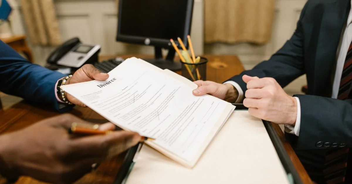 Gros plan des mains échangeant des documents de divorce lors de procédures légales au bureau.