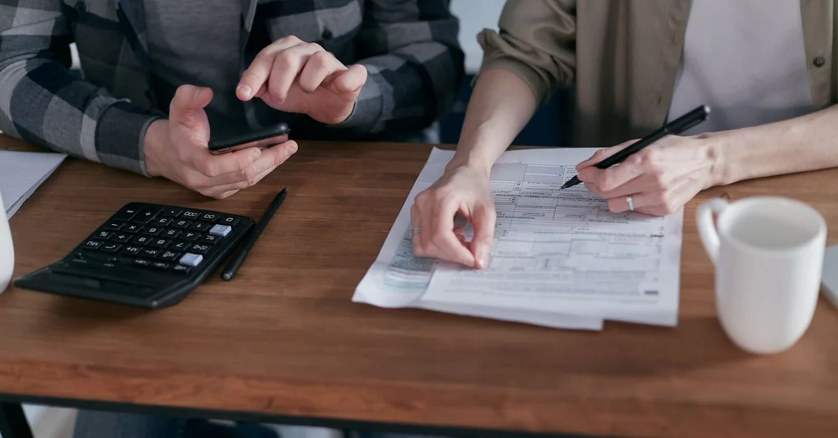 Deux personnes travaillant ensemble sur des formulaires fiscaux avec une calculatrice à un bureau en bois.