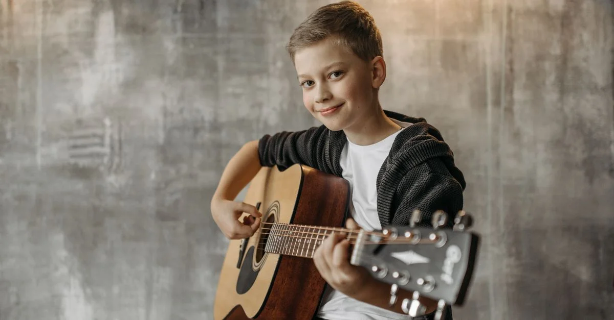 Un jeune garçon joyeux jouant de la guitare acoustique devant un mur en béton.