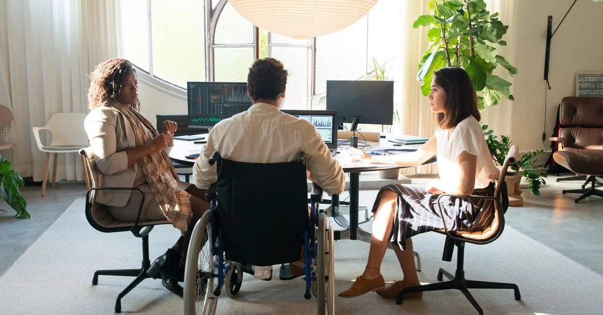 Équipe diversifiée ayant une discussion dans un bureau moderne avec lumière naturelle. Comprend un membre utilisant un fauteuil roulant.