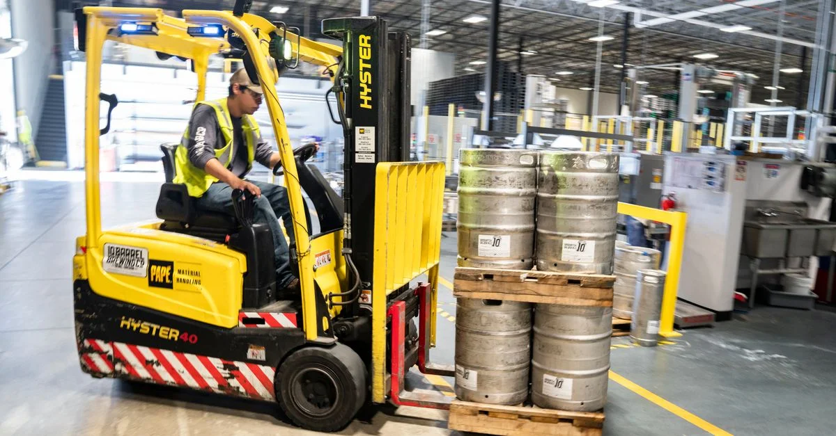 Opérateur de chariot élévateur dans un entrepôt déplaçant des fûts de bière pour distribution.