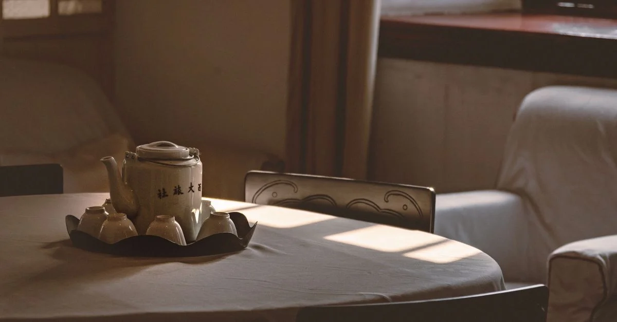 Une table sereine avec une théière et des tasses, baignant dans la douce lumière de l'après-midi, évoque chaleur et tranquillité.