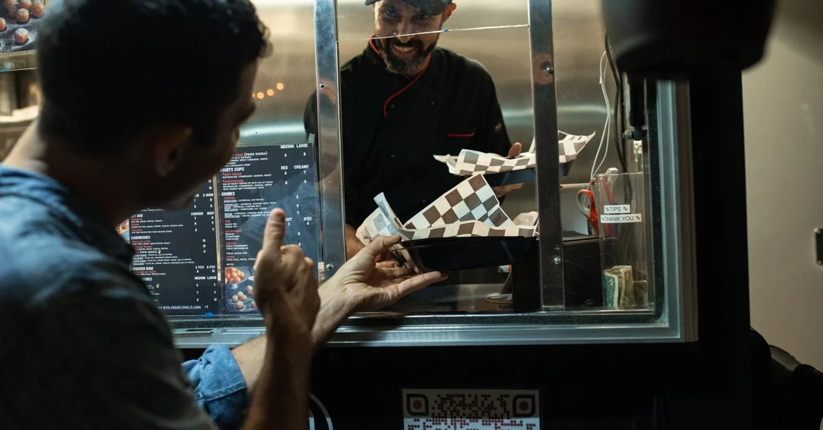 Un homme commande de la nourriture à un chef à l'intérieur d'un food truck de rue la nuit.