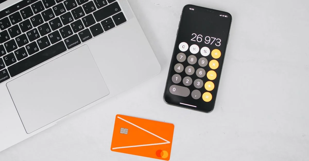 Un ordinateur portable, un smartphone affichant une calculatrice et une carte de crédit sur une table blanche.