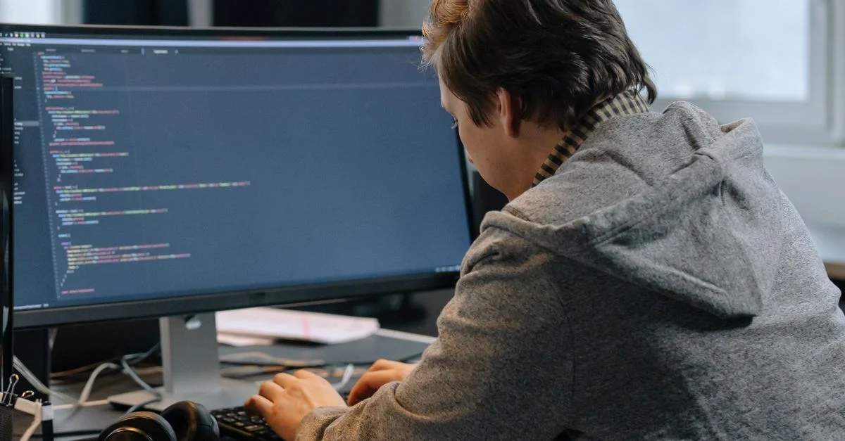 Un homme en hoodie code sur un bureau avec de grands écrans dans un bureau.