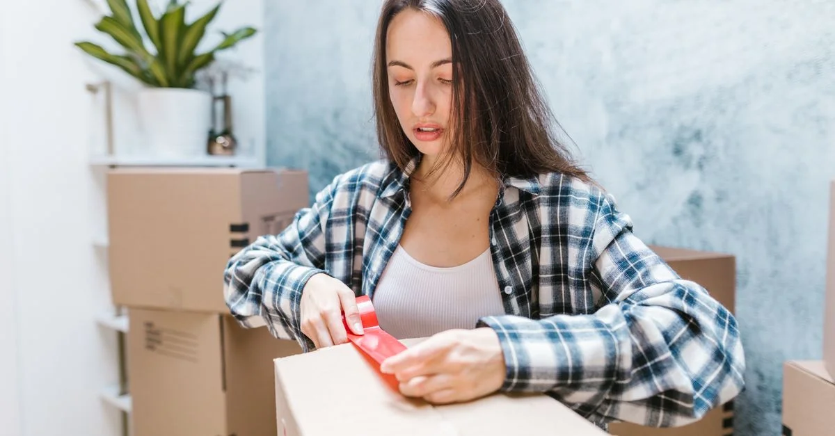 Femme scotchant des cartons pour un déménagement dans un cadre intérieur chaleureux.