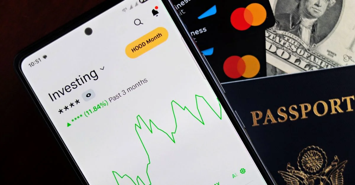Smartphone affichant une application d'investissement, avec des cartes de crédit, de l'argent liquide et un passeport à proximité, symbolisant la finance
