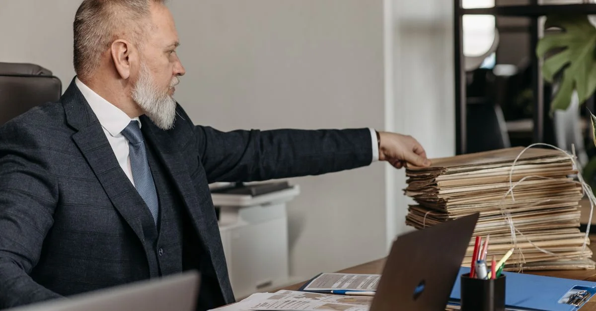 Homme d'affaires mature atteignant une pile de dossiers sur son bureau dans un environnement de bureau moderne.