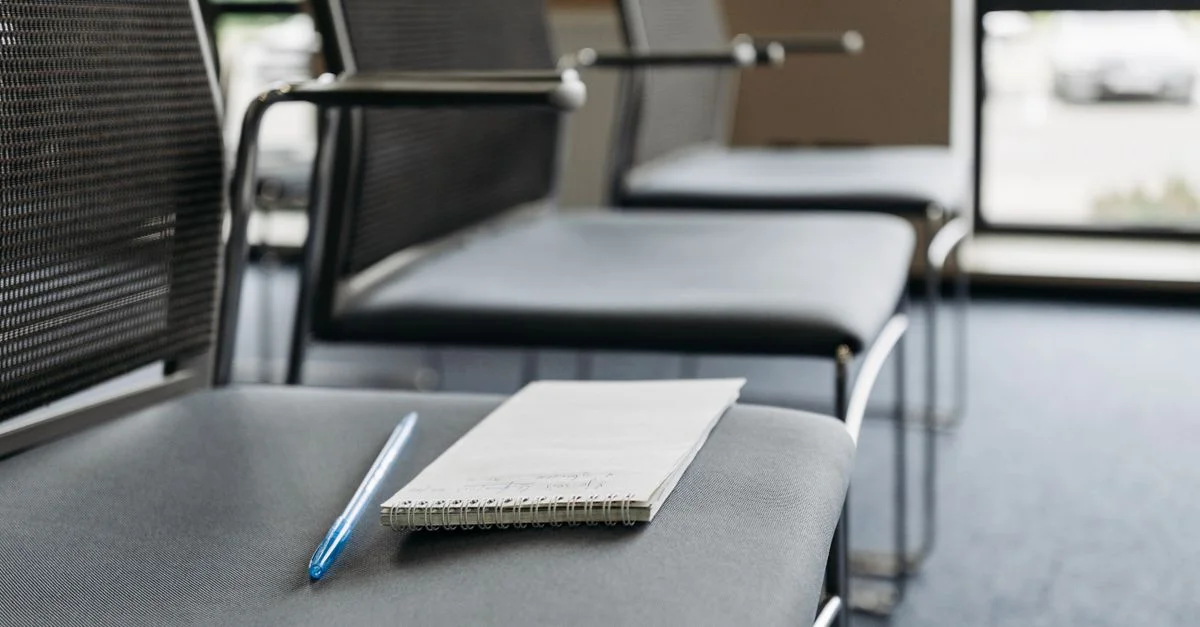 Gros plan sur des chaises avec un cahier et un stylo dans une salle de réunion bien éclairée.