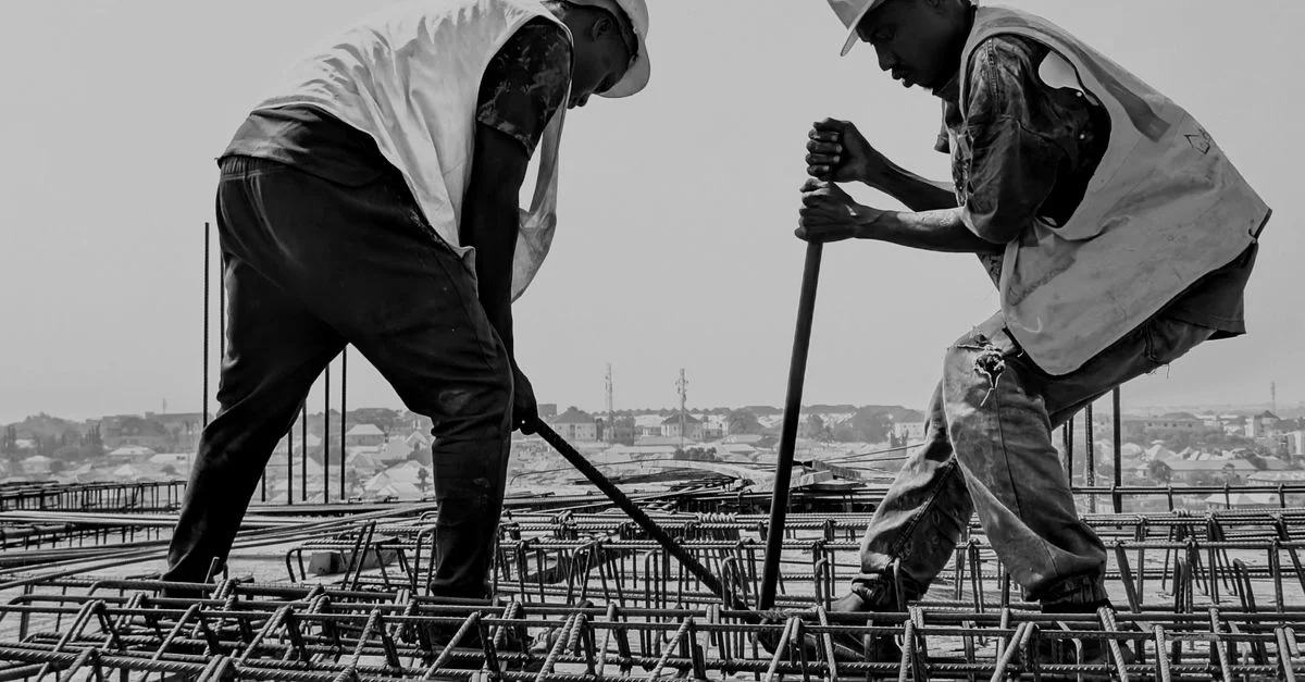 Image en noir et blanc de deux travailleurs de construction renforçant des barres d'acier sur un chantier.