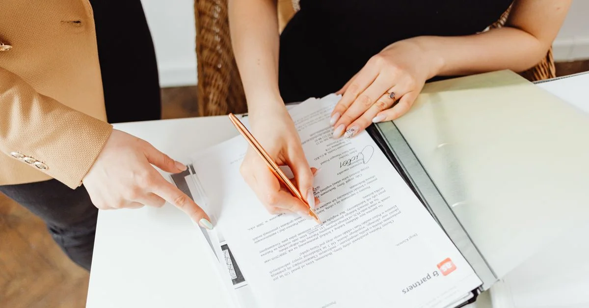 Deux femmes signant des documents importants à un bureau, illustrant le travail d'équipe.