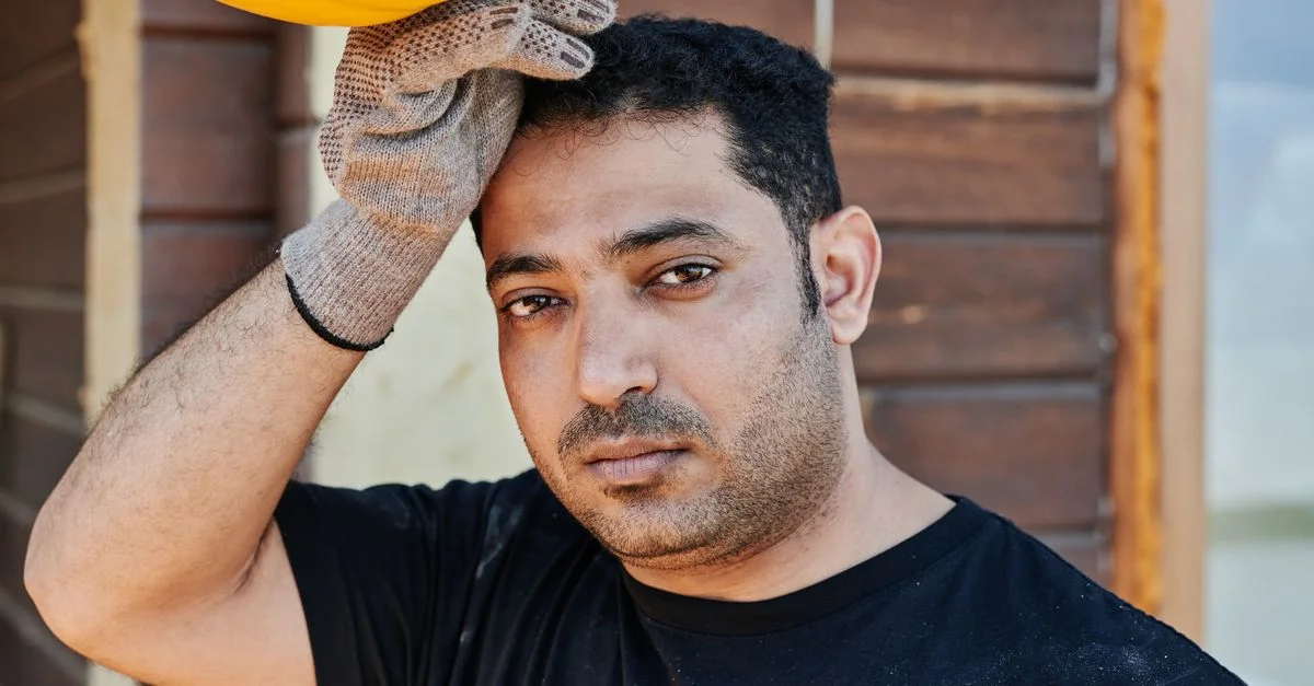 Portrait en gros plan d'un ouvrier du bâtiment se reposant, tenant son casque de chantier. Main gantée, expression pensive.