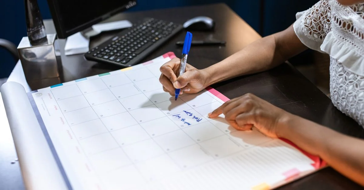 Personne écrivant des notes importantes dans un calendrier de bureau avec un stylo, dans un bureau.