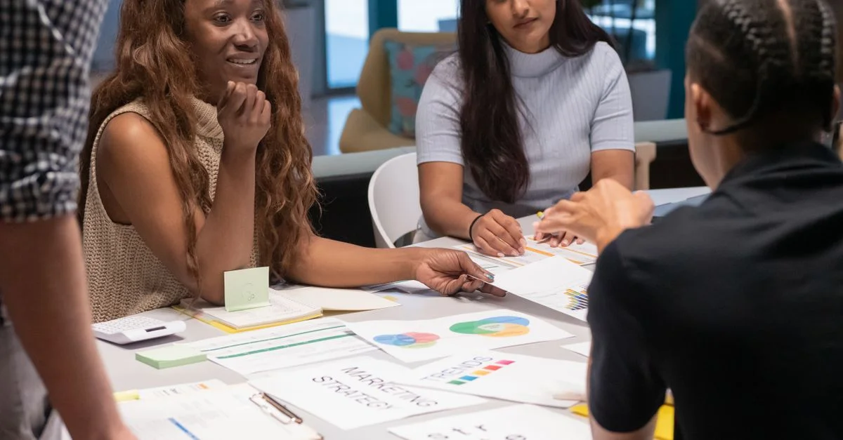Groupe de collègues discutant des stratégies de marketing autour d'une table dans un espace de travail contemporain.