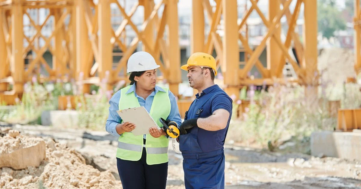 Des travailleurs de la construction engagés dans une discussion sur un chantier portant des équipements de sécurité.