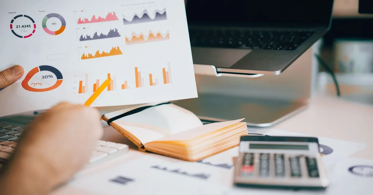Gros plan sur des mains analysant des données financières avec des graphiques, un ordinateur portable et une calculatrice.