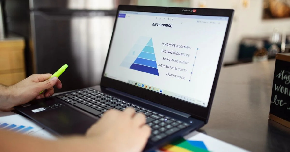 Une personne analyse des données commerciales sur un ordinateur portable, utilisant un graphique en pyramide et des rapports financiers.