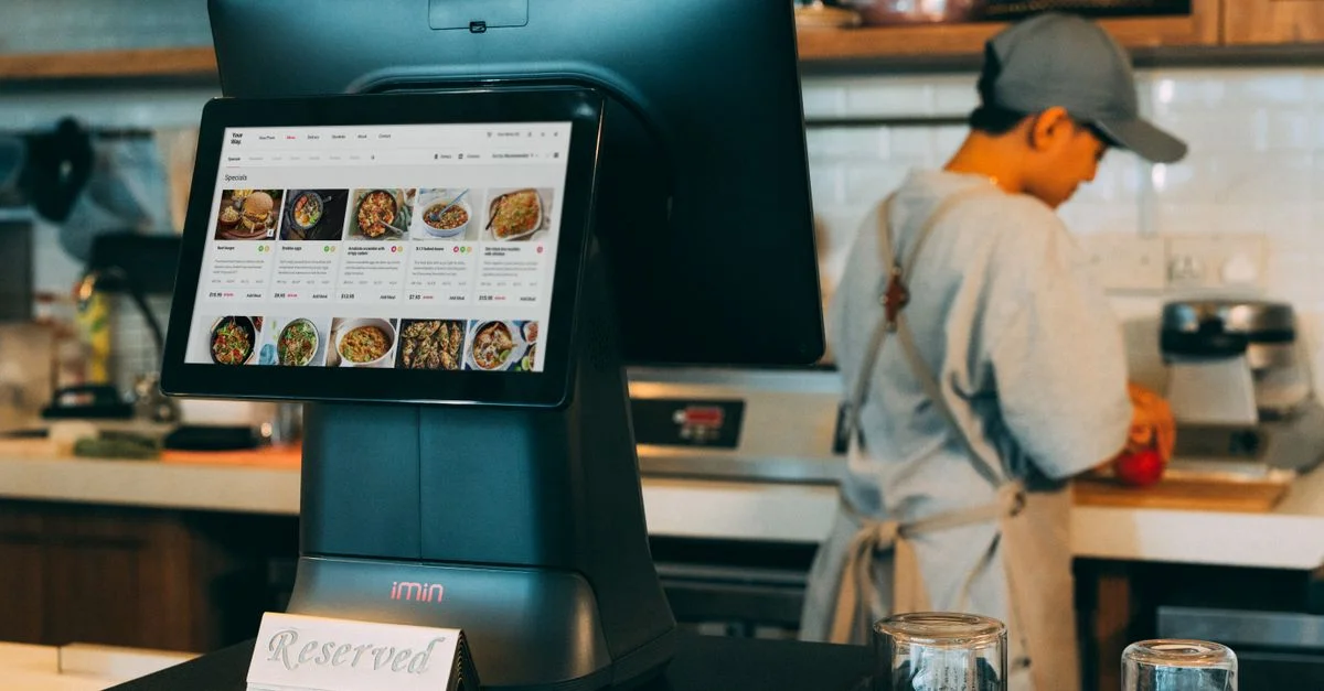 Système de commande numérique dans une cuisine de restaurant avec un écran tactile et un chef au travail.