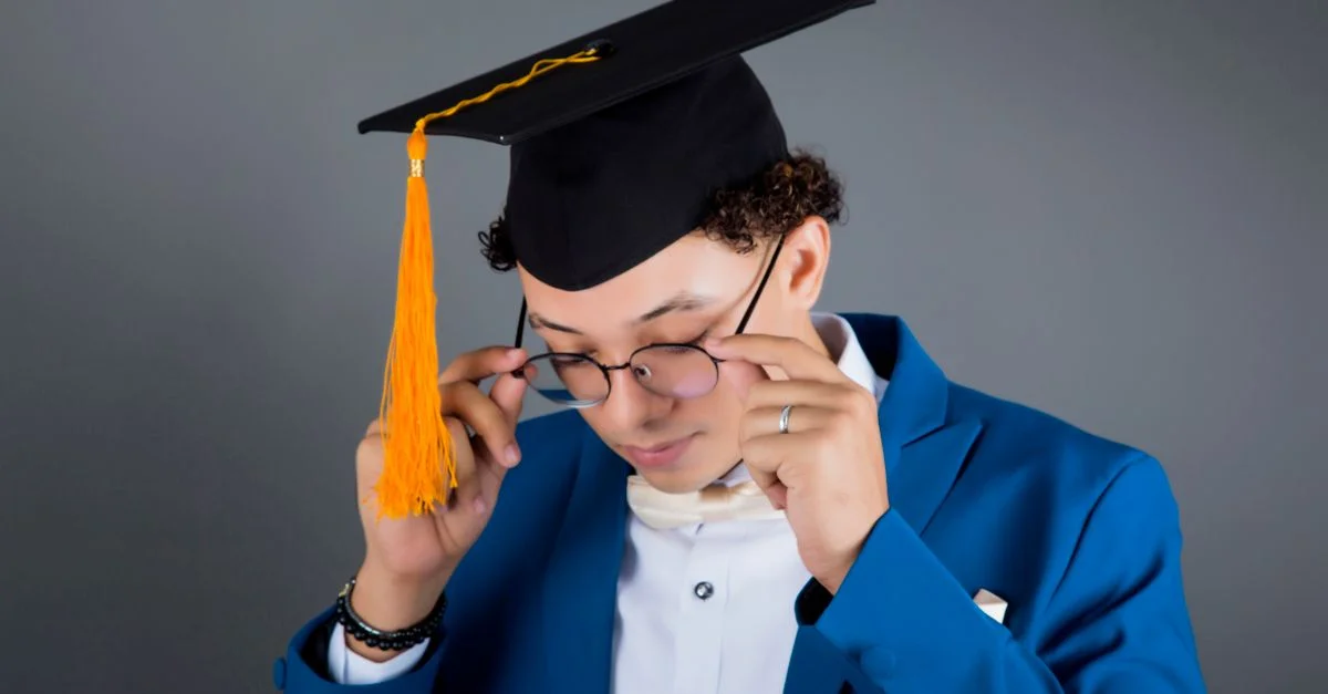 Portrait d'un jeune homme coiffé d'une toque de diplômé, ajustant ses lunettes et célébrant sa réussite.