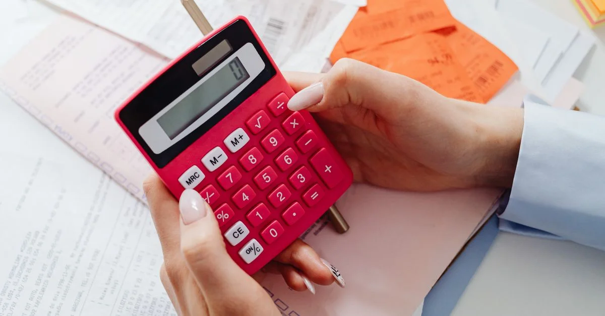 Gros plan sur des mains tenant une calculatrice rouge, gérant des finances avec des documents et des reçus.