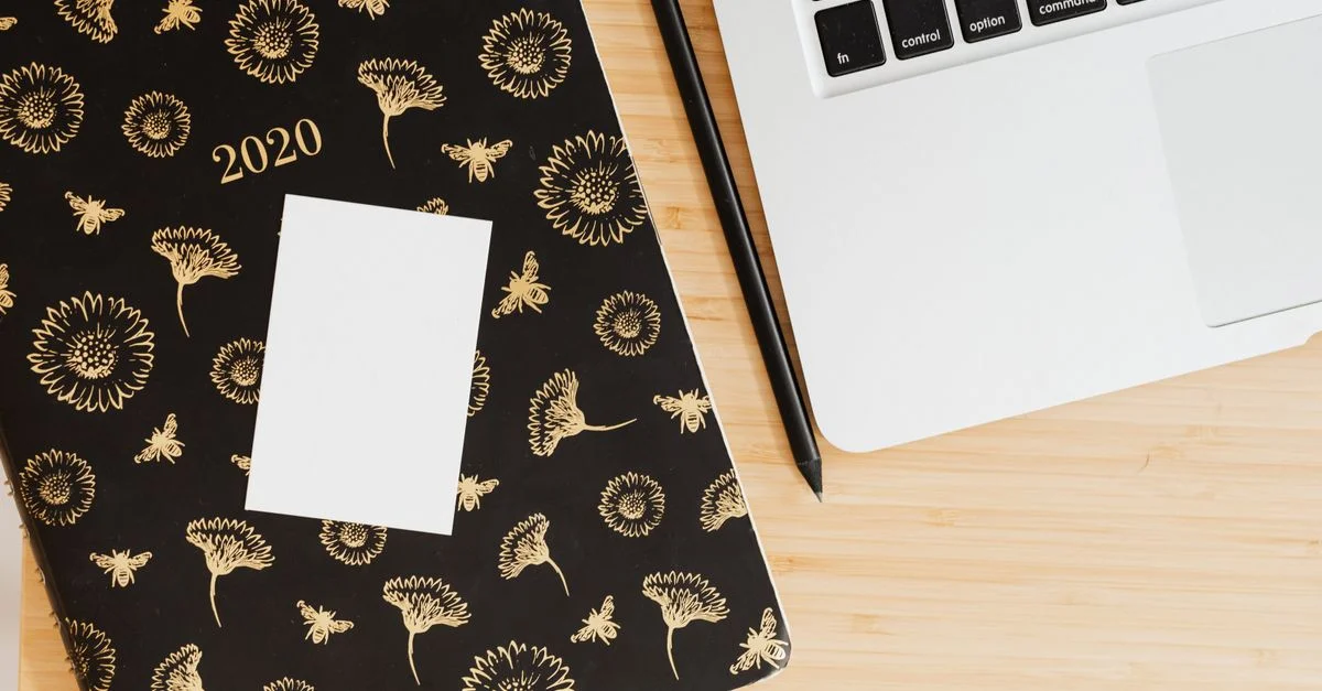 Vue de dessus d'un espace de travail moderne avec un planificateur floral, un stylo et un ordinateur portable sur un bureau en bois.