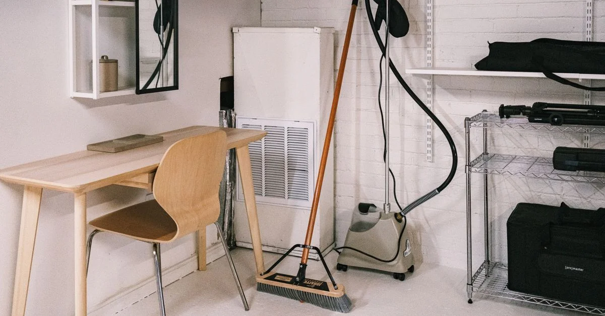 Un espace de bureau à domicile bien rangé, comprenant un bureau en bois, une chaise, un balai et du matériel de nettoyage.