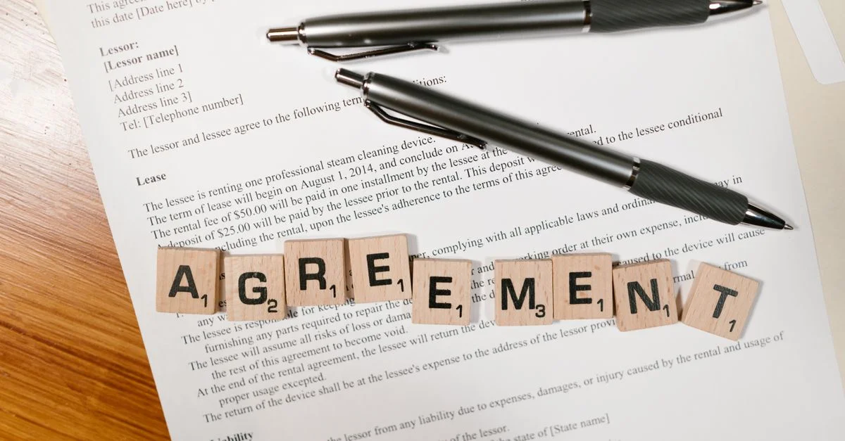 Un document avec des lettres de Scrabble orthographiant 'ACCORD' et deux stylos, symbolisant la signature d'un contrat.