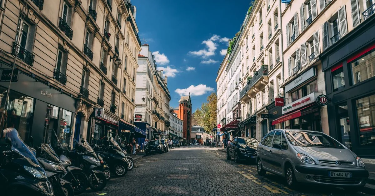 Scène de rue pittoresque à Paris avec une architecture classique, des motos garées et des voitures.